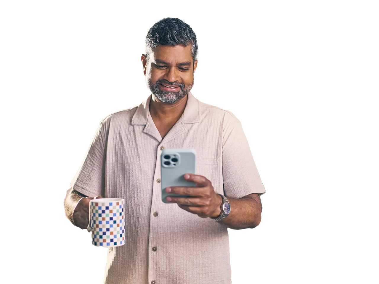 A man stands in a kitchen and looks at his phone with a smile.